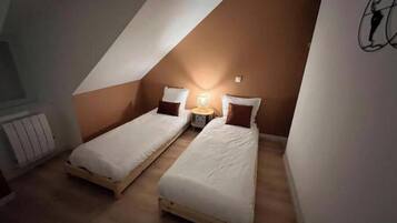 A small, triangular attic bedroom with two single beds, a nightstand, and a wall-mounted lamp.