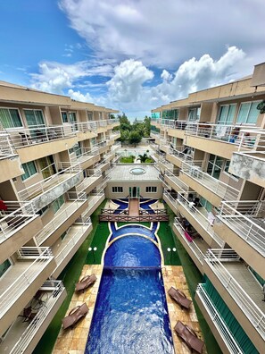 A multi-story hotel with a central swimming pool, balconies, and a view of the sky. - Muito Ventilado, Wifi 300mb, Até 5 pessoas + Pet (Praia de Cumbuco Caucaia)