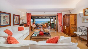 Ein Wohnzimmer mit einem weißen Sofa, roten Kissen, einem Couchtisch und Meerblick.