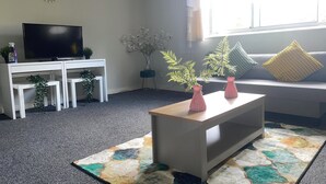 A living room with a TV, white furniture, a colorful rug, and a window with a view.