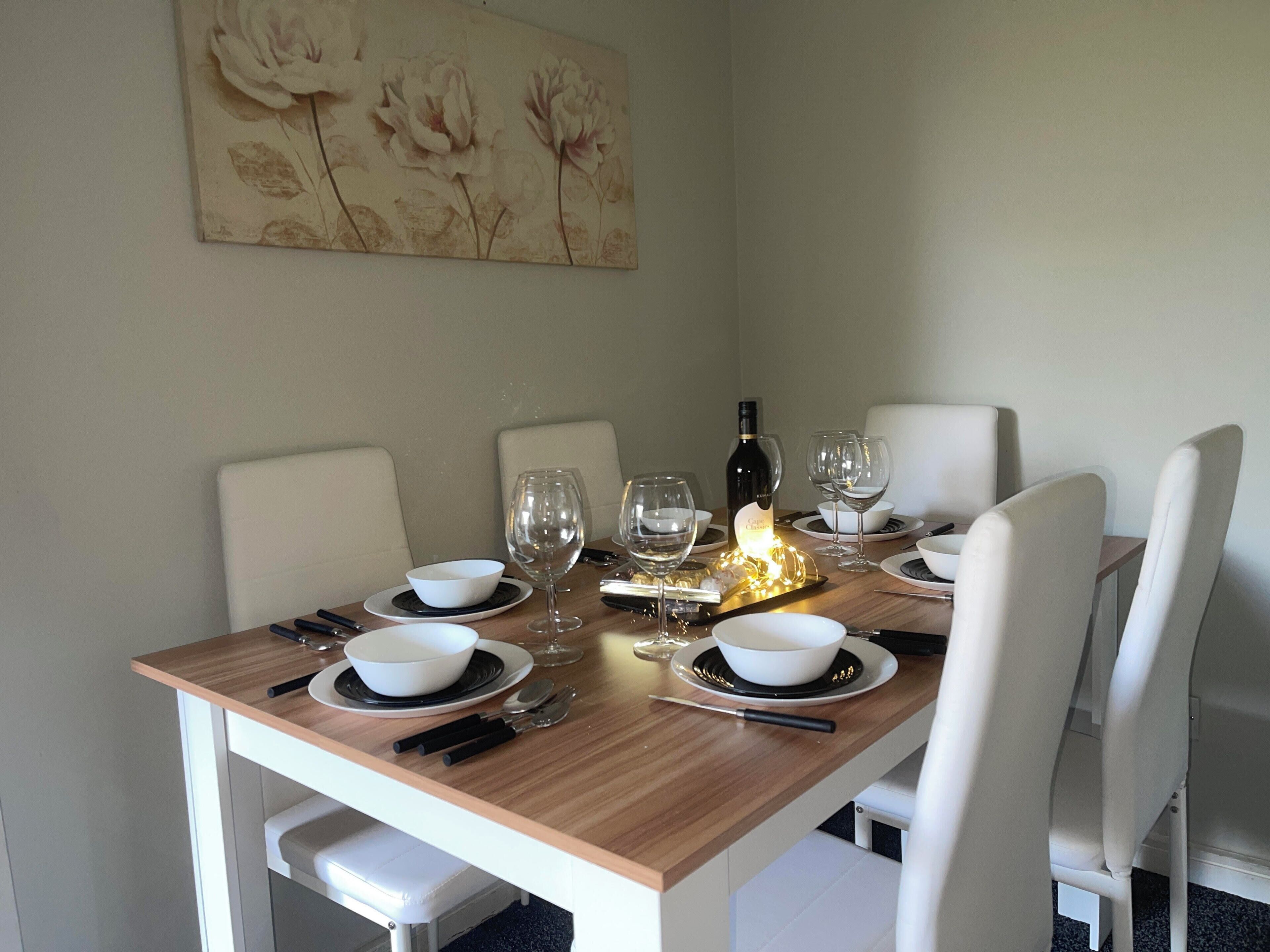 A dining table set with white bowls, wine glasses, and cutlery, a bottle of wine, and a decorative light.