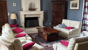 Un salon avec des canapés de couleur beige, une table basse en bois, une cheminée et un grand meuble.