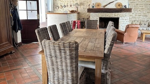 Un coin repas rustique avec une table en bois et des chaises en osier, une cheminée en pierre et un sol carrelé.