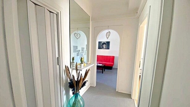A hallway with a mirror, a vase with dried plants, and a red sofa in the background. - Complete and bright apartment in Monfalcone  (Monfalcone)