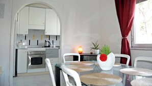 A modern kitchen with white cabinets, a built-in oven, and a dining area with a glass table and white chairs. - Complete and bright apartment in Monfalcone  (Monfalcone)