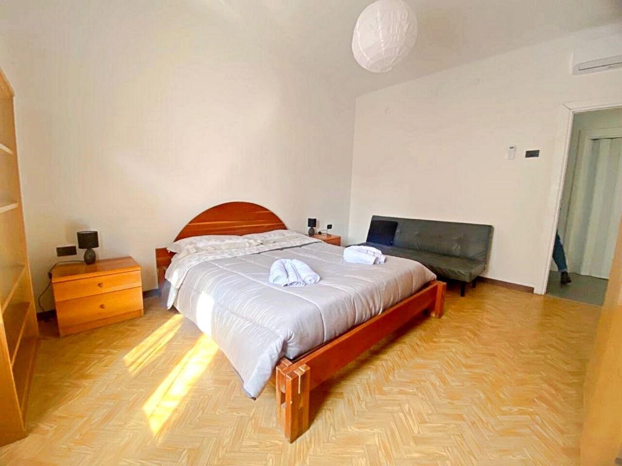 Une chambre à coucher avec un lit en bois, une table de chevet, une commode et un canapé gris.