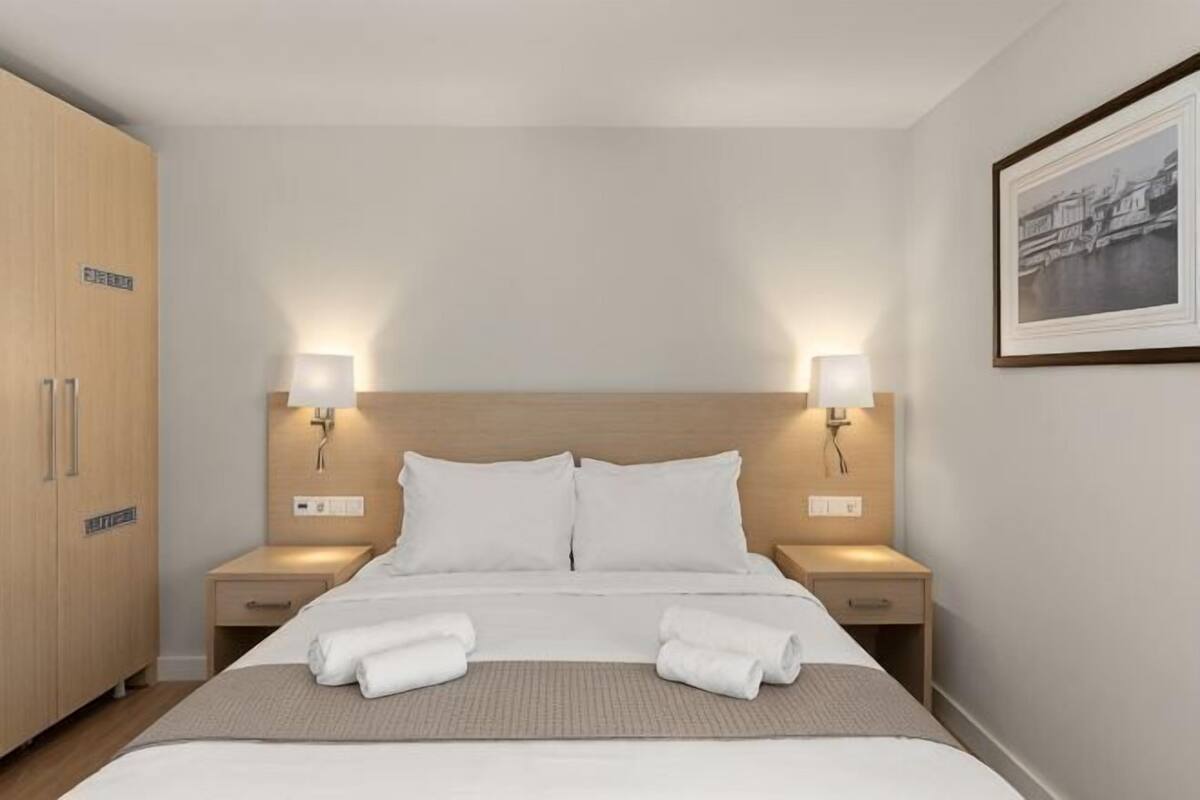 A hotel room with a large bed, two bedside tables with lamps, a wooden wardrobe, and a framed picture on the wall.