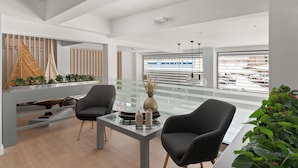 A modern interior with a glass table, two chairs, a wooden slatted wall, and a view of an airport. - Gallery Central Piraeus Port (Piraeus)