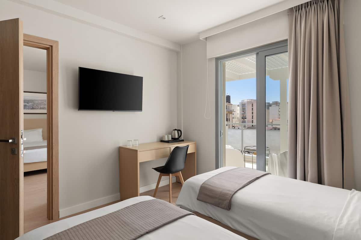 A hotel room with two beds, a desk, a chair, a TV, and a large window with curtains.