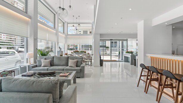 A modern, spacious living area with a sofa set, a coffee table, and a bar area with stools. - Gallery Central Piraeus Port (Piraeus)