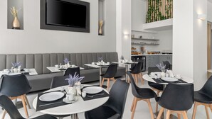 A modern dining area with a grey sofa, black chairs, and a flat-screen TV mounted on the wall. - Gallery Central Piraeus Port (Piraeus)