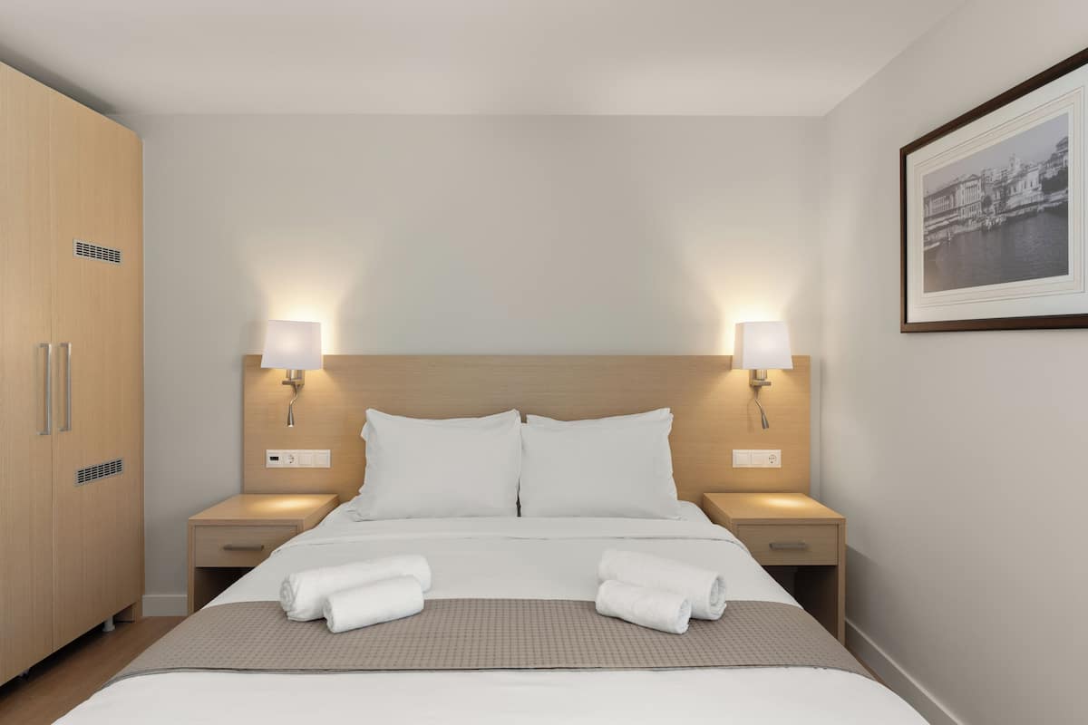 A hotel room with a large bed, two bedside tables, a wardrobe, and a framed picture on the wall.