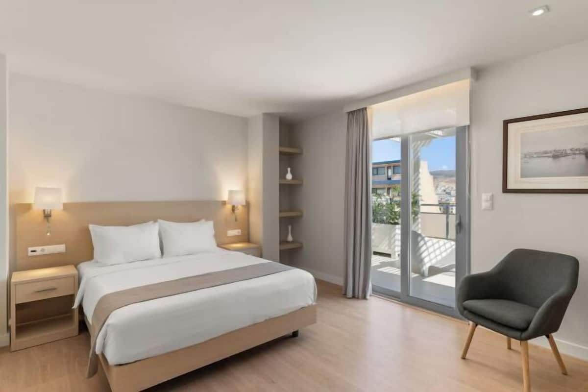 A modern hotel room with a large bed, bedside lamps, a chair, and a balcony with a view.