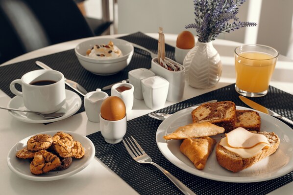 A breakfast table with a cup of coffee, a glass of orange juice, a bowl of cereal, a plate of pastries, and a small vase with flowers. - Gallery Central Piraeus Port (Piraeus)