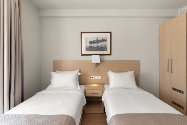 A hotel room with two single beds, a nightstand, a framed picture on the wall, and a wardrobe.