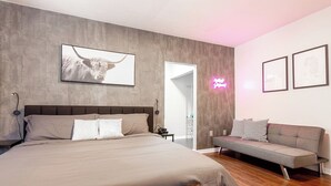 Un dormitorio con una cama grande, un sofá, un televisor y un letrero de neón.