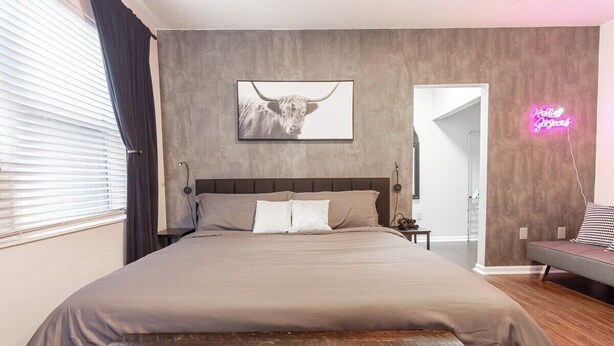 Un dormitorio moderno con una cama grande, una obra de arte en la pared de un toro y un letrero de neón.