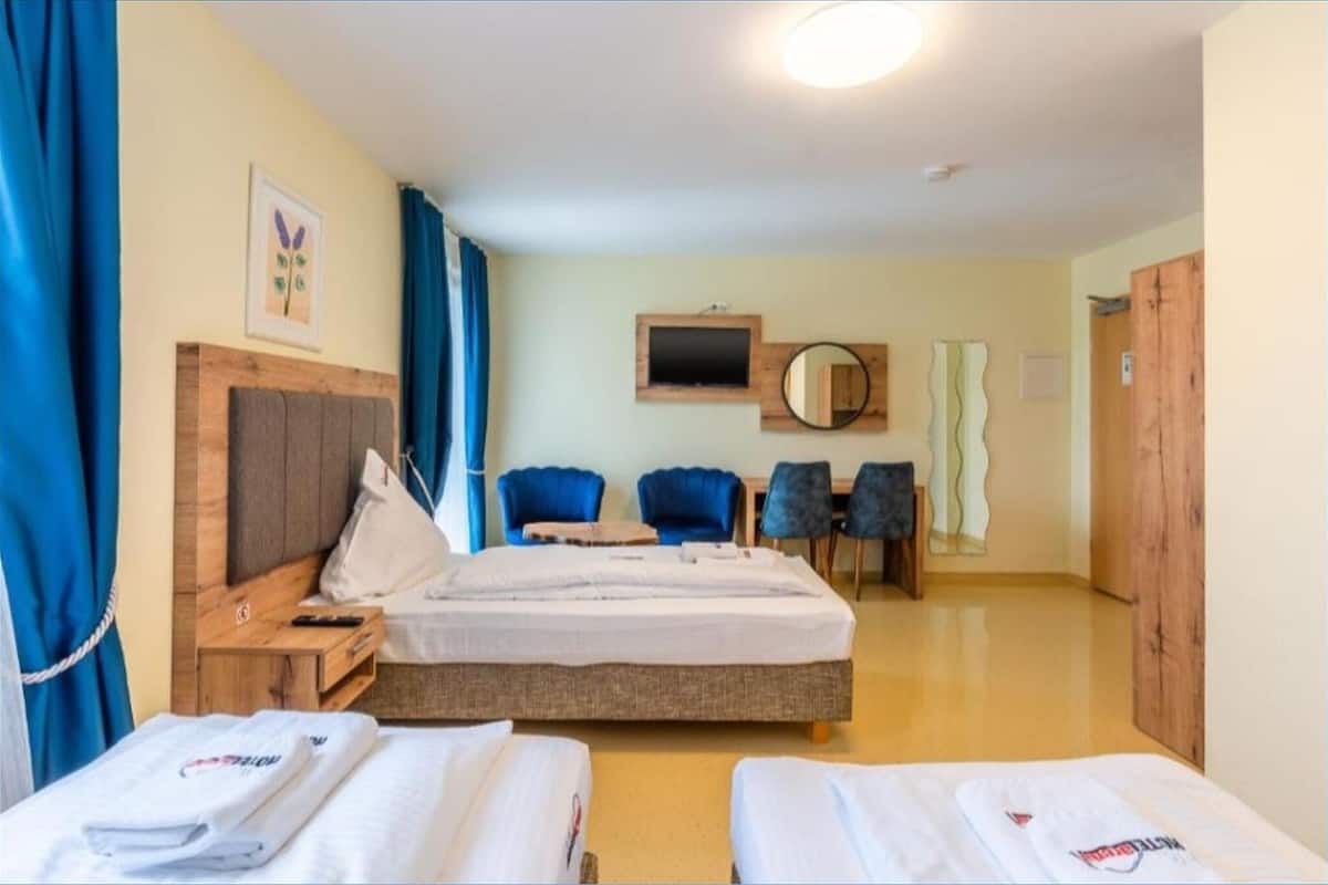 A hotel room with a bed, two chairs, a desk, a mirror, and a television.