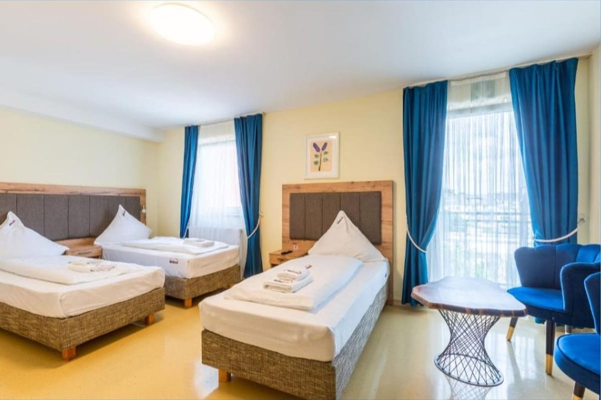 A hotel room with two single beds, a small table, and a chair.