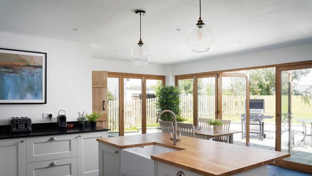 A modern kitchen with white cabinetry, a wooden countertop, and a large window. - 4-bed Cottage - Pets With Garden & Wood Burner (Helston)