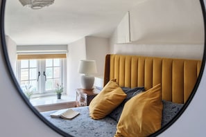 A bedroom with a bed, a bedside table with a lamp, a window with a view, and a door.