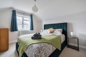 Ein Schlafzimmer mit einem Bett, einem Nachttisch, einer Lampe, einem Fenster mit Vorhängen und einer Heizung.
