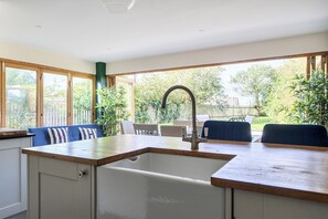 A kitchen with a built-in sink, wooden countertop, and a view of the backyard through large windows. - 4-bed Cottage - Pets With Garden & Wood Burner (Helston)