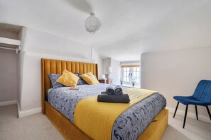 A bedroom with a bed, a chair, a window, and a ceiling light. - 4-bed Cottage - Pets With Garden & Wood Burner (Helston)