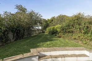 A grassy backyard with a stone retaining wall and dense foliage. - 4-bed Cottage - Pets With Garden & Wood Burner (Helston)
