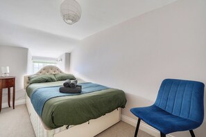 A bedroom with a bed, a chair, a bedside table, and a window. - 4-bed Cottage - Pets With Garden & Wood Burner (Helston)