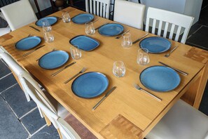 A wooden dining table set with blue plates, silverware, and clear glasses. - 4-bed Cottage - Pets With Garden & Wood Burner (Helston)
