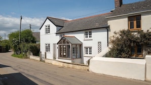 A two-story house with a white exterior, a dark roof, and a small front porch. - 4-bed Cottage - Pets With Garden & Wood Burner (Helston)