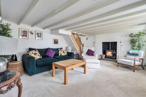 A living room with a sofa, a wooden coffee table, a fireplace, and a staircase. - 4-bed Cottage - Pets With Garden & Wood Burner (Helston)
