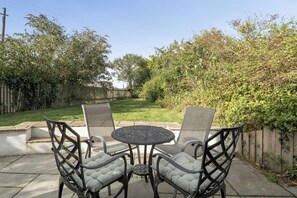 An outdoor patio with a round table and four chairs, surrounded by a wooden fence and greenery. - 4-bed Cottage - Pets With Garden & Wood Burner (Helston)
