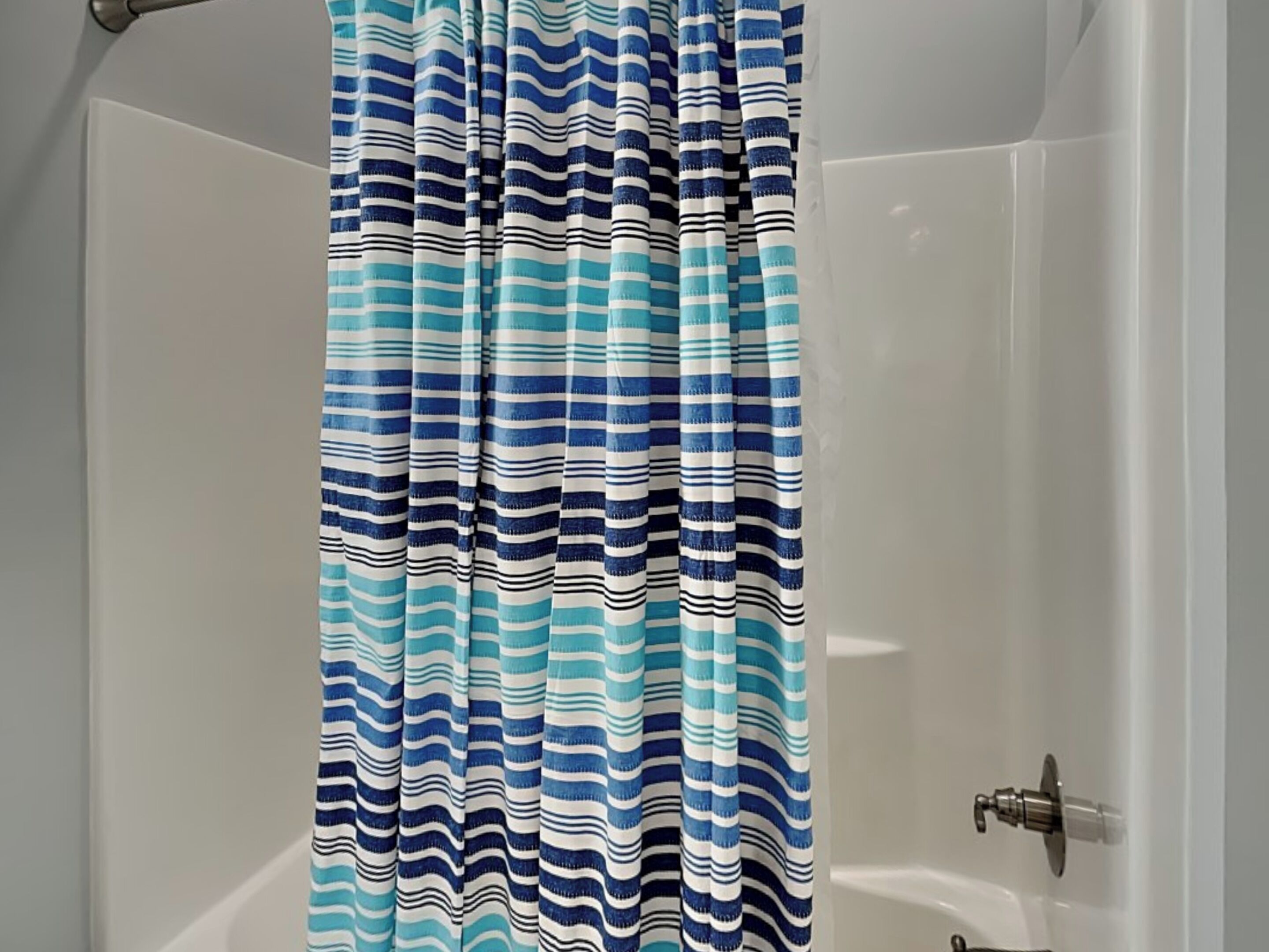 Cortina de ducha con estampado azul y blanco a rayas en un baño con bañera blanca y grifo de cromo.