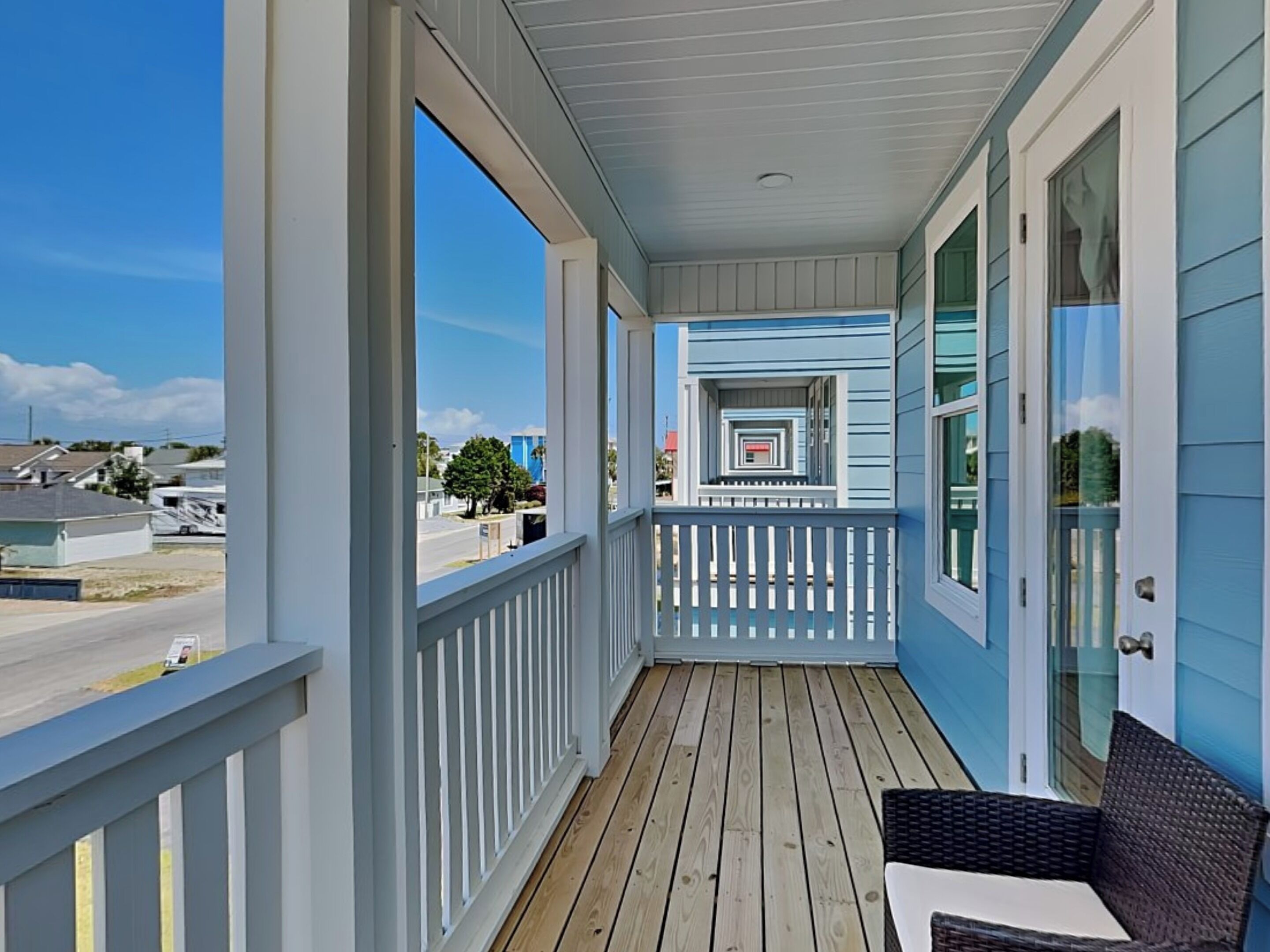 A covered porch with a wooden deck, white railings, and a wicker chair.