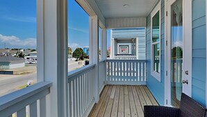 A covered porch with a wooden deck, white railings, and a wicker chair. - The Blue Pearls by Resort Collection (Panama City Beach)