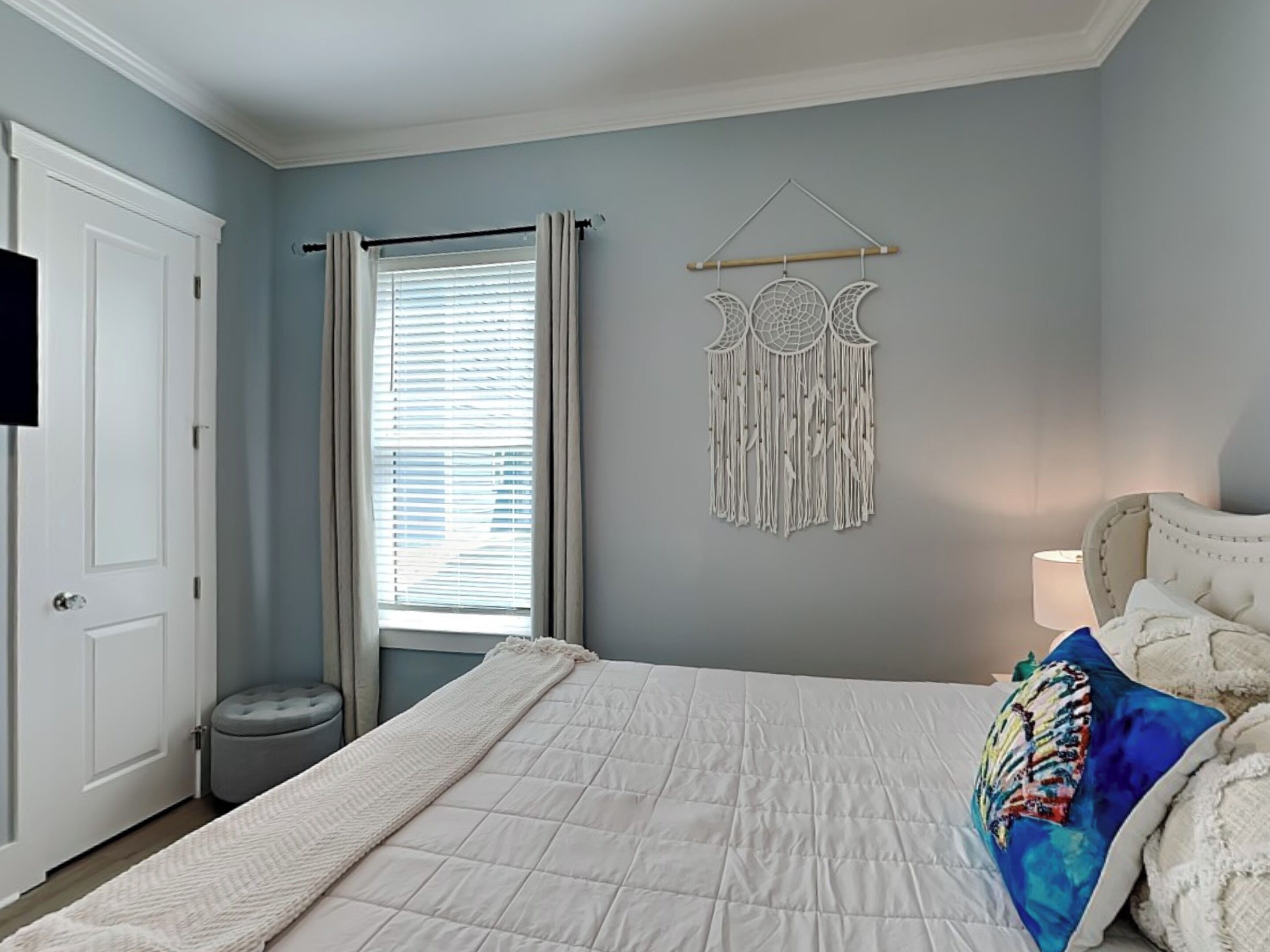 A bedroom with a bed, a bedside lamp, a wall hanging, and a door.