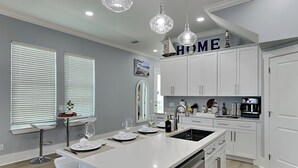 A modern kitchen with white cabinetry, a central island, and pendant lighting. - The Blue Pearls by Resort Collection (Panama City Beach)