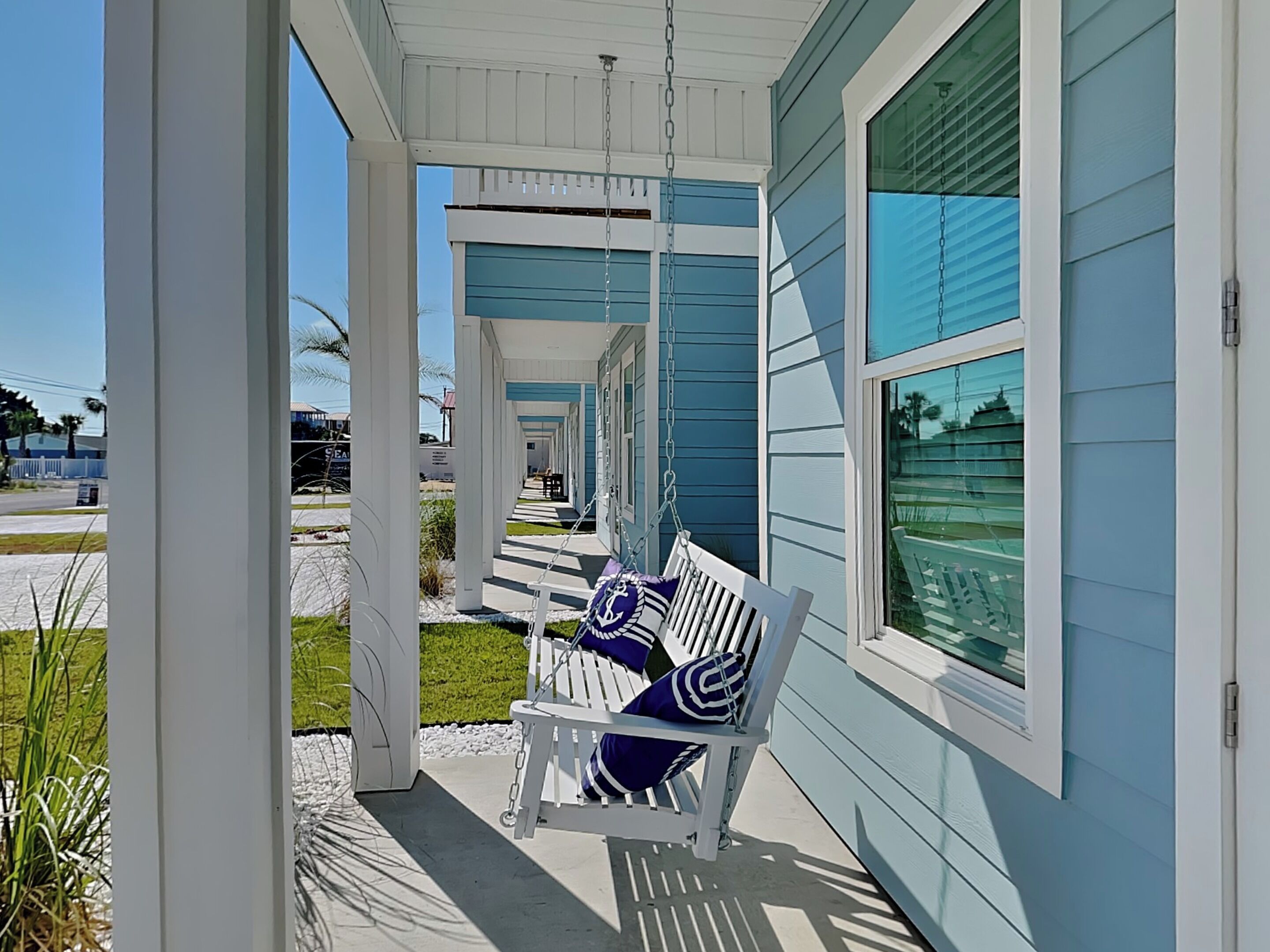 A porch with a white swing chair and a blue and white striped cushion.
