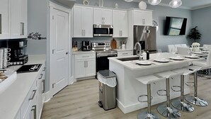 A modern kitchen with white cabinetry, stainless steel appliances, a central island with bar stools, and pendant lighting. - The Blue Pearls by Resort Collection (Panama City Beach)