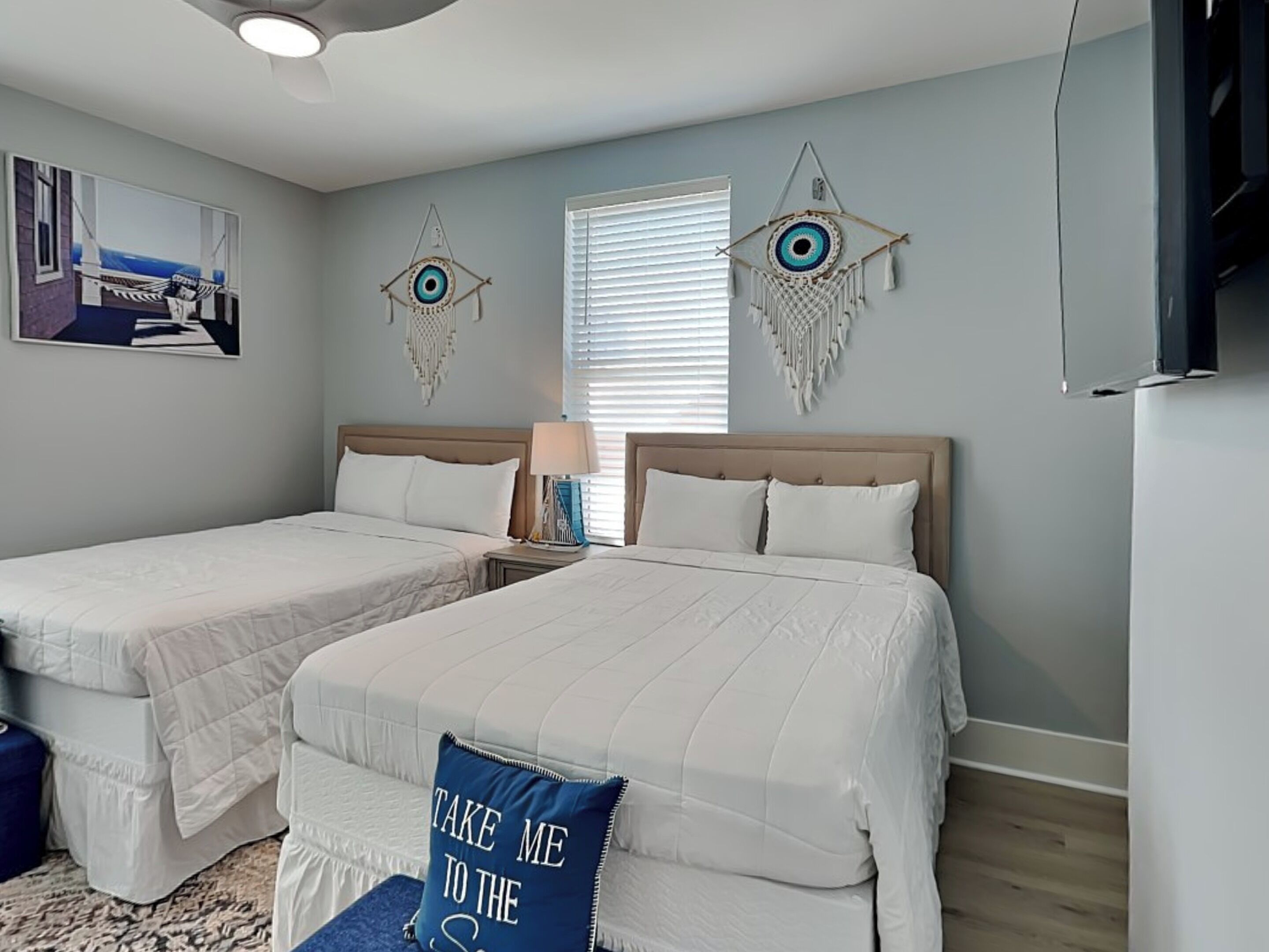 Un dormitorio con dos camas, ventilador de techo, ventana con persianas y decoración en las paredes.