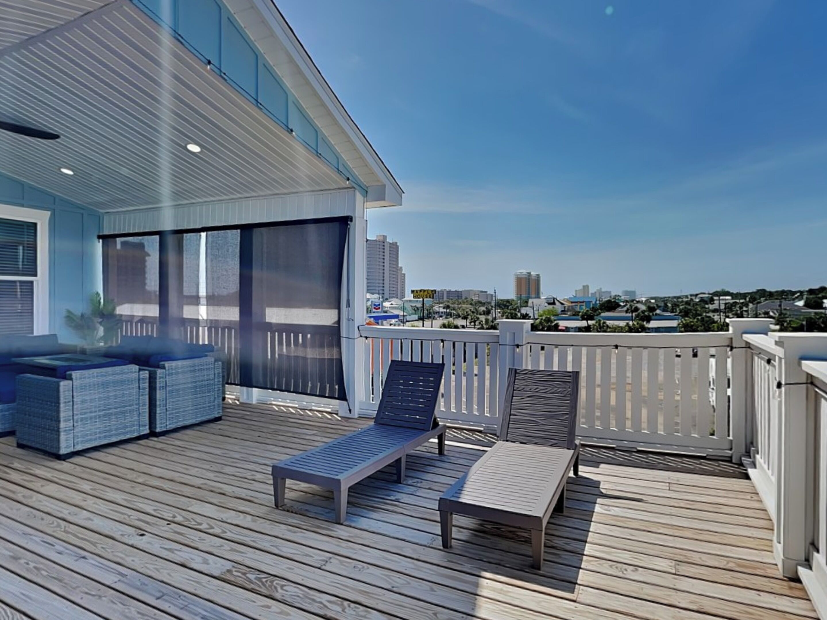 Een houten terras met buitenmeubels, waaronder een bank en twee loungestoelen, met uitzicht op een stadsgezicht.