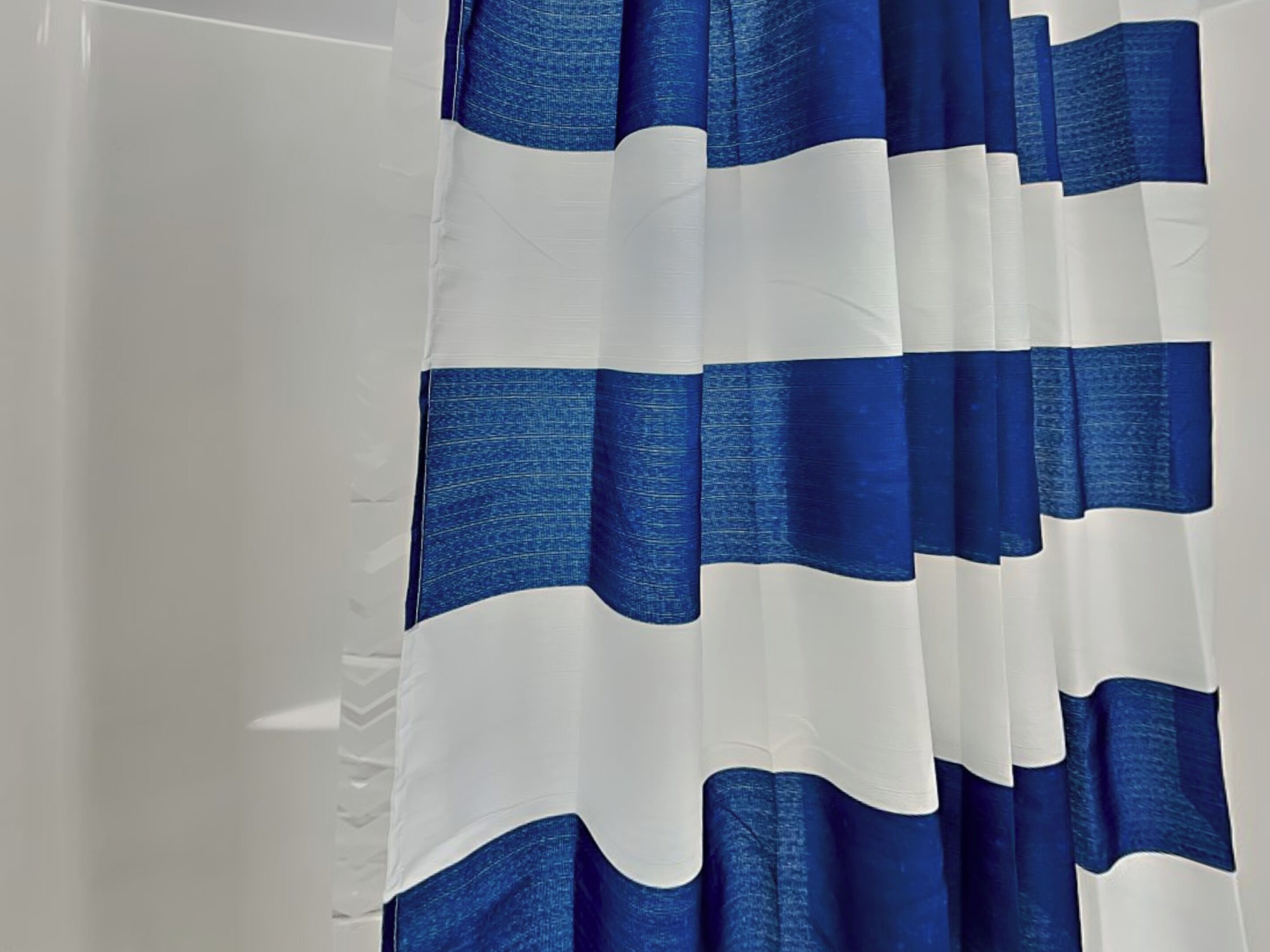 Un baño con cortina de ducha blanca y rayas horizontales azules.