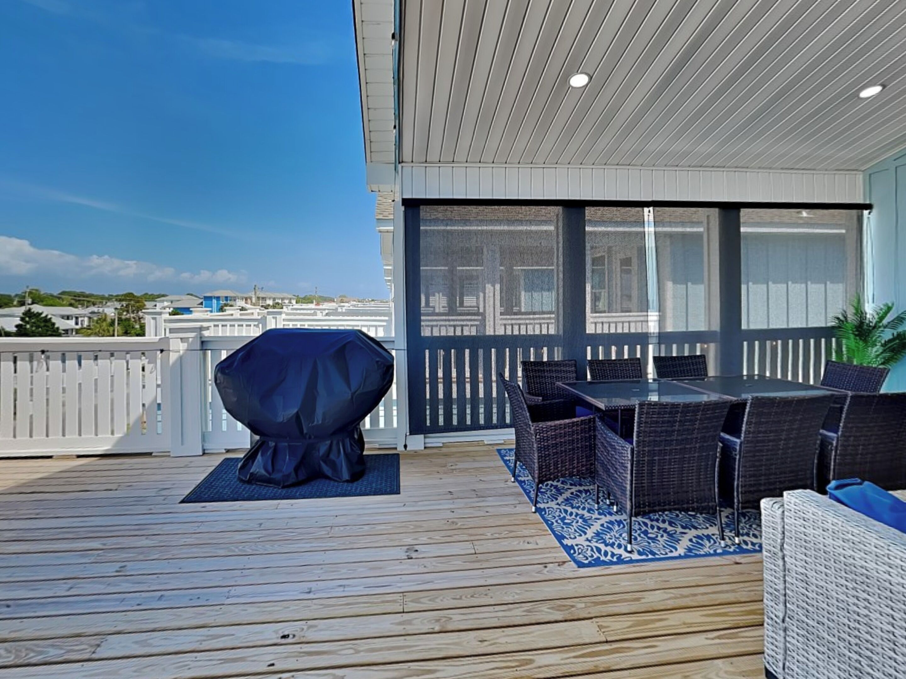Eine Holzterrasse mit überdachtem Grill, Sitzgelegenheiten im Freien und Blick auf die Stadt.