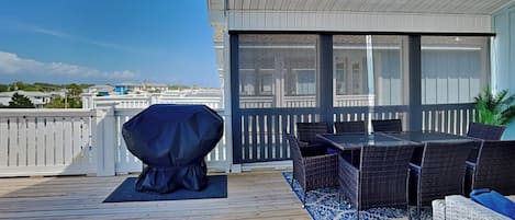A wooden deck with a covered grill, outdoor seating, and a view of the city.