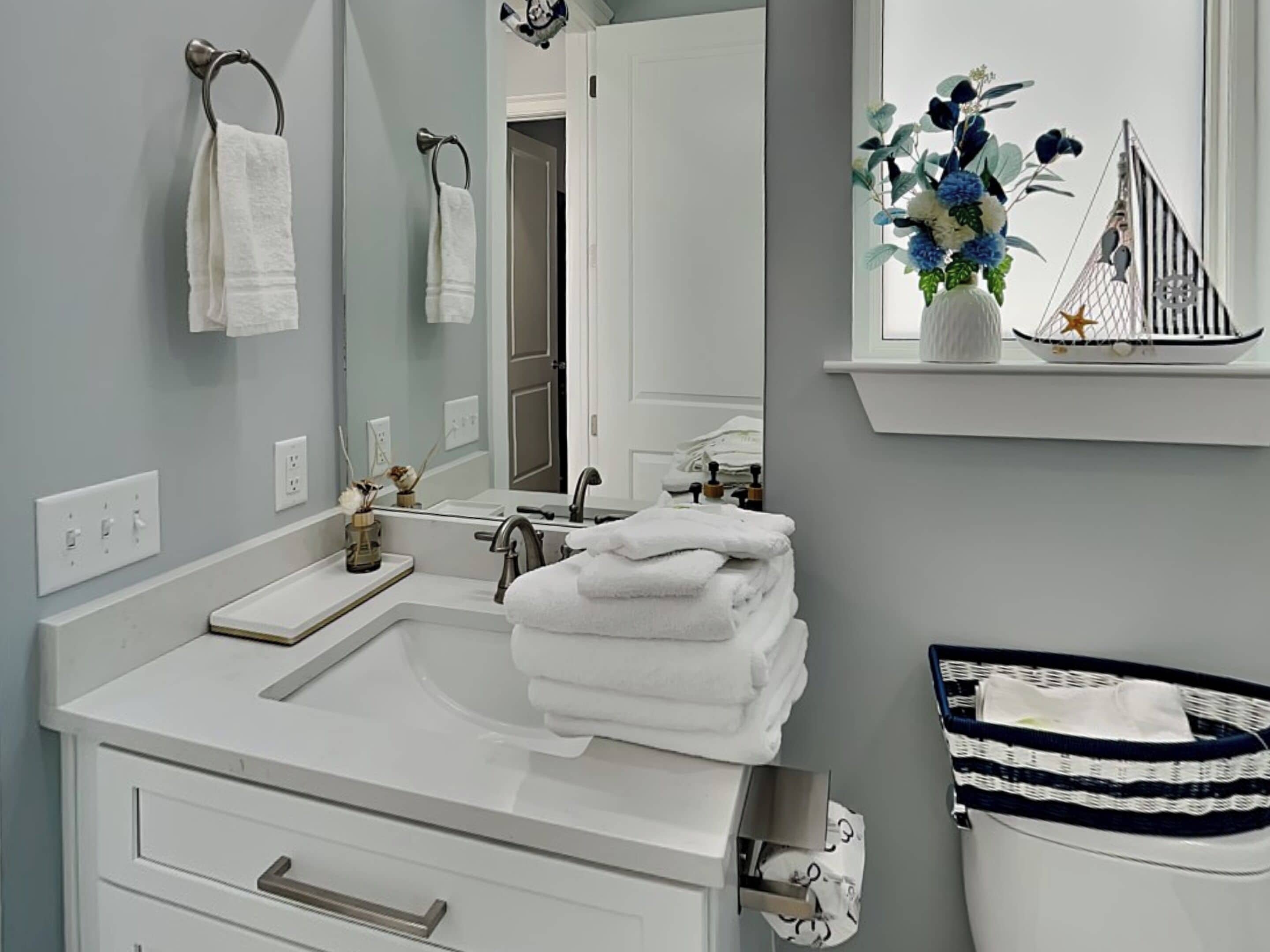Un baño con un lavamanos blanco, un espejo y un ventanal con un jarrón decorativo.