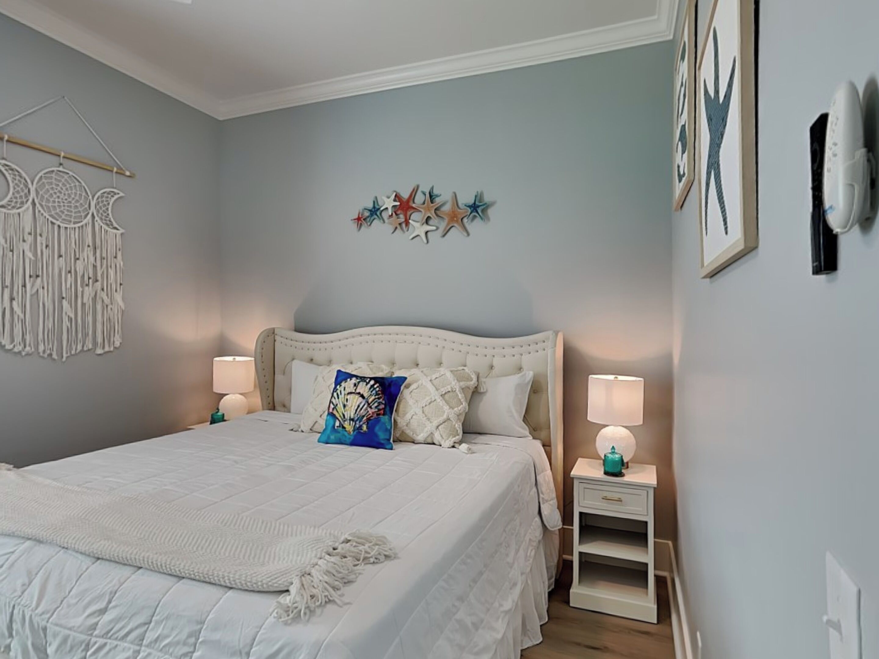 Une chambre avec un grand lit, deux tables de chevet avec des lampes, une décoration murale en forme d’étoile et un attrape-rêves.