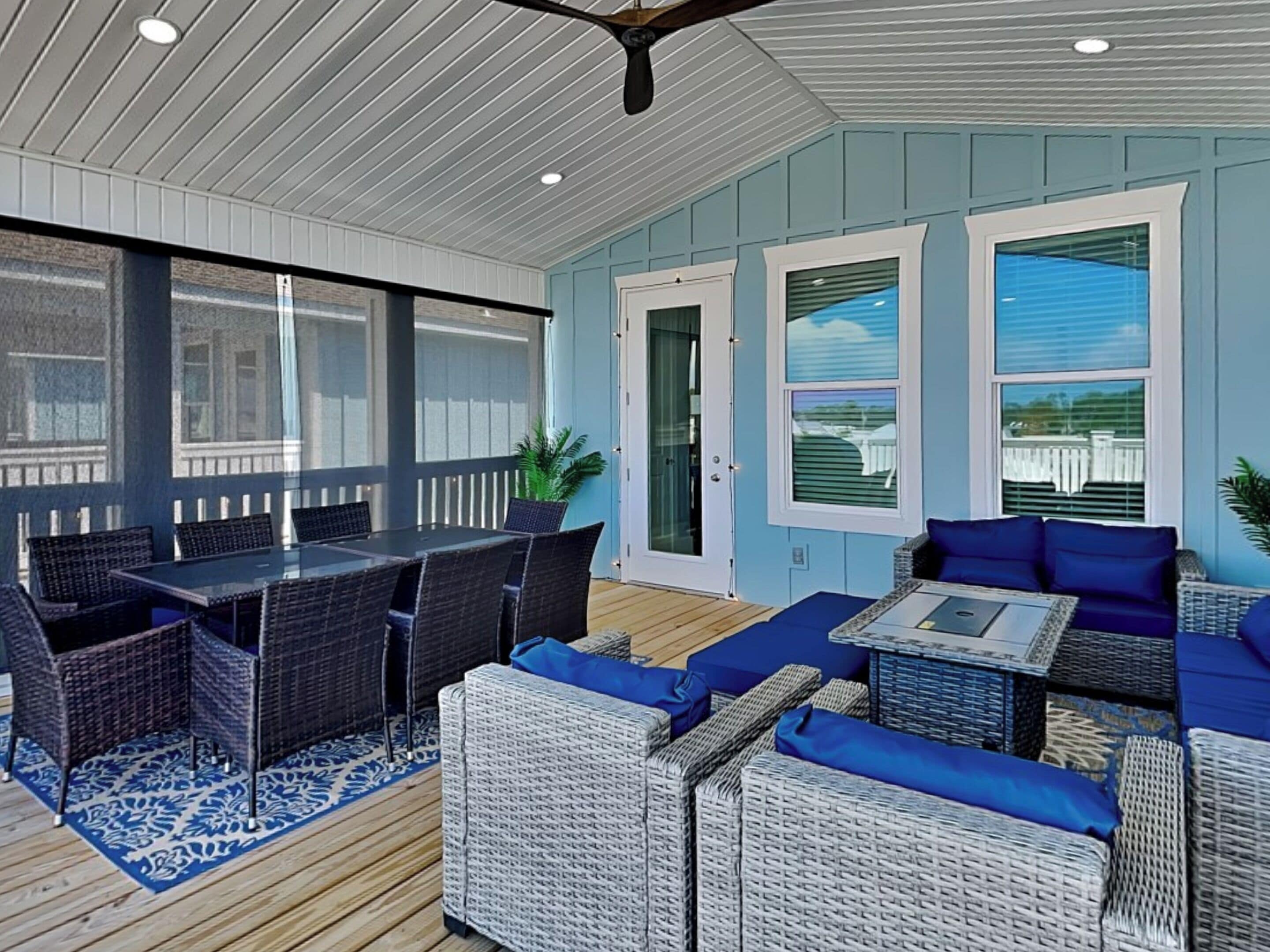 An outdoor patio with wicker furniture, a glass-top table, and a blue patterned rug.