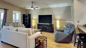 Una sala de estar con sofá, sillón, televisor y ventilador de techo.